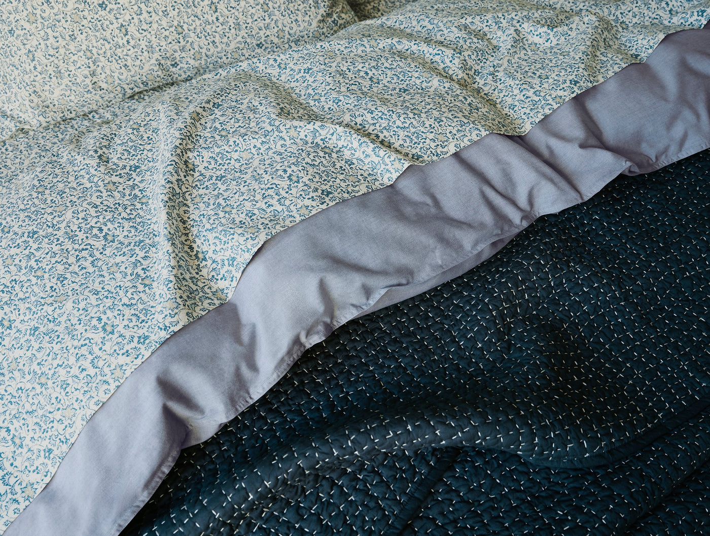 Close-up of teal quilted texture meeting floral printed layers with slate satin trim detail.