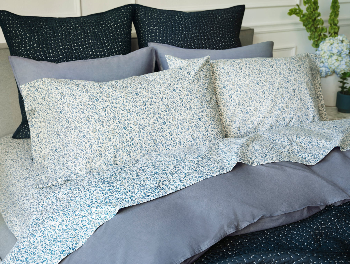 Close-up of blue floral print percale pillowcases layered over slate duvet on styled bed.