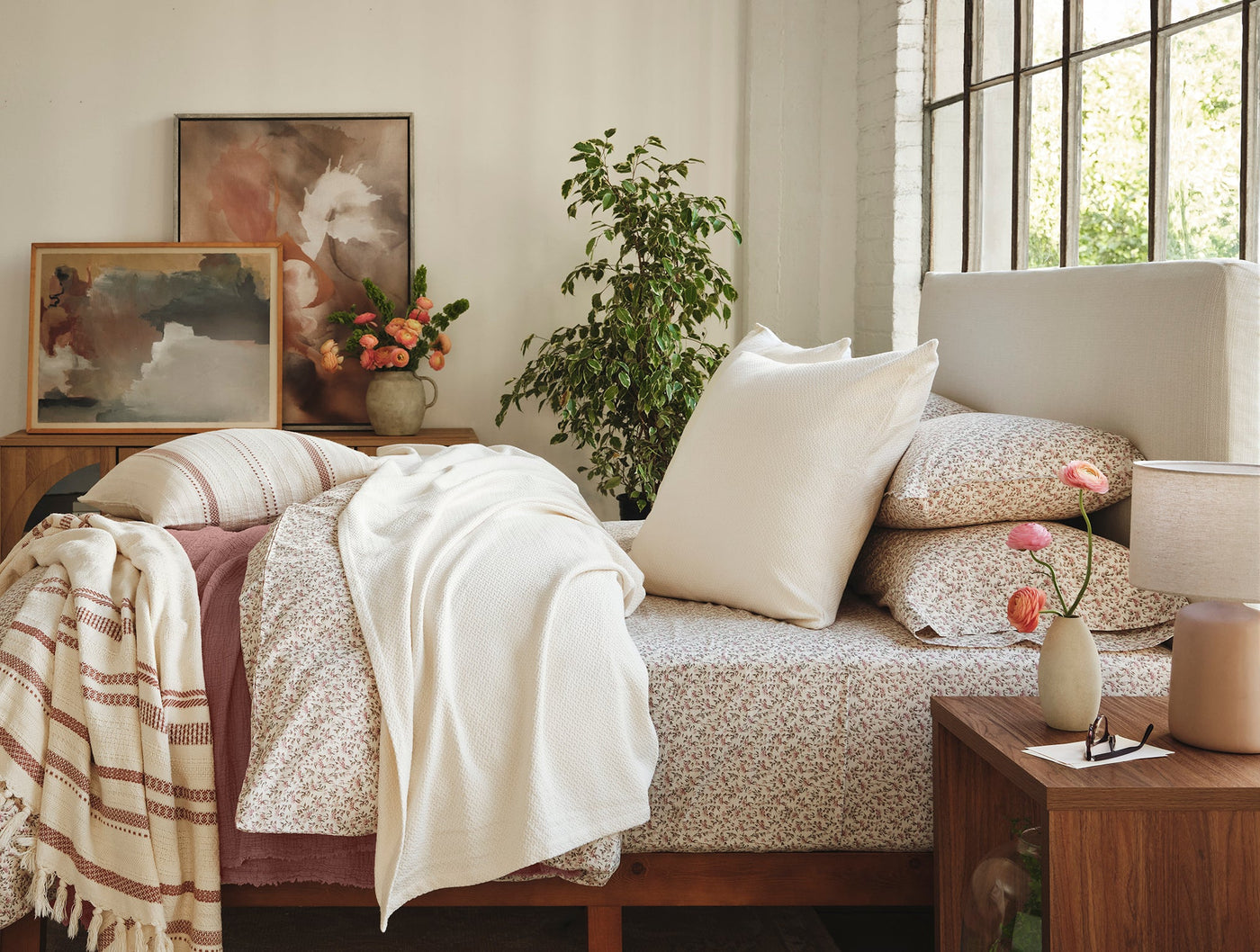 Cream and rust striped Coyuchi Bonita throw draped over bed corner in warm, plant-filled bedroom.