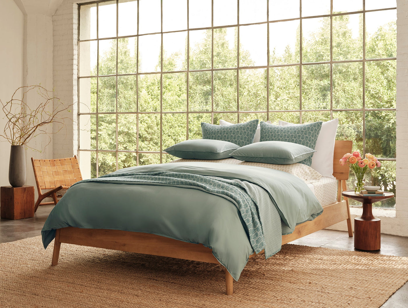 Sage green Coyuchi Mirada Matelasse blanket draped across a styled bed in a light-filled room.