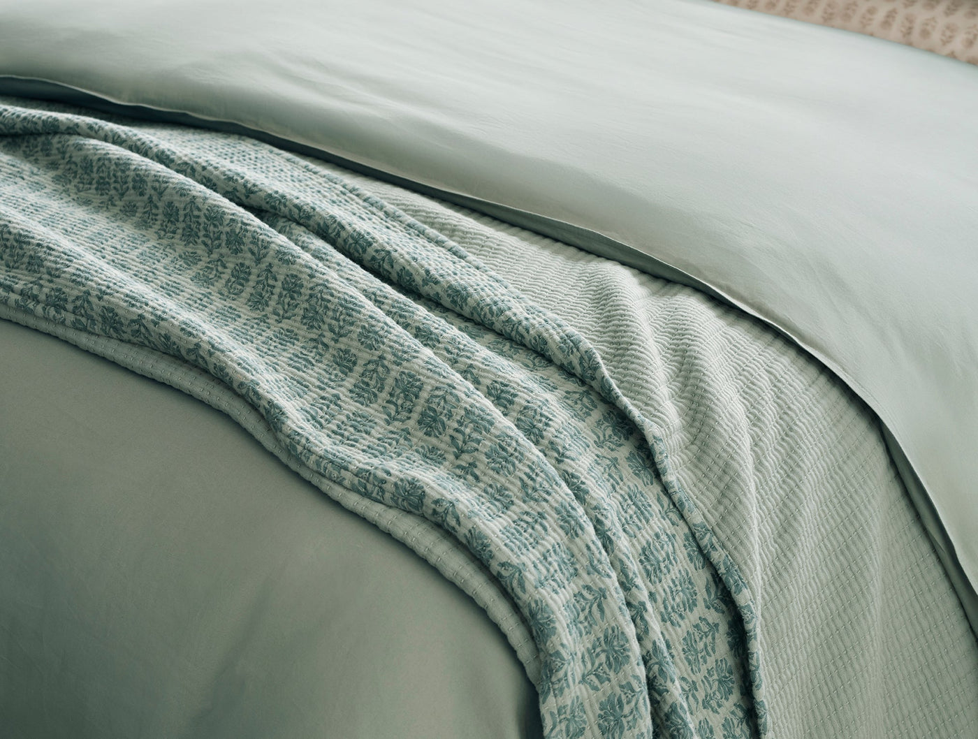 Close-up of Coyuchi Mirada Matelasse blanket in sage, draped over sage bedding.