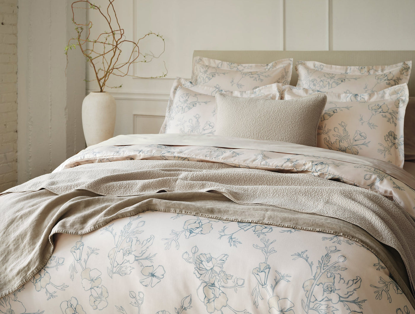 Ivory matelasse blanket draped over floral-print bedding in a softly lit bedroom.