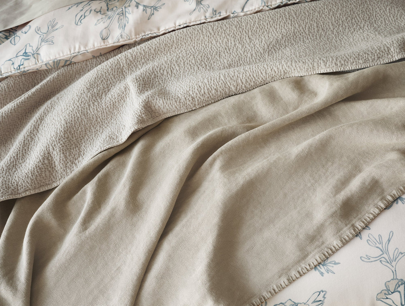 Close-up of Coyuchi Cascade Matelassé blanket in natural, showing draped texture and blanket stitch hem.
