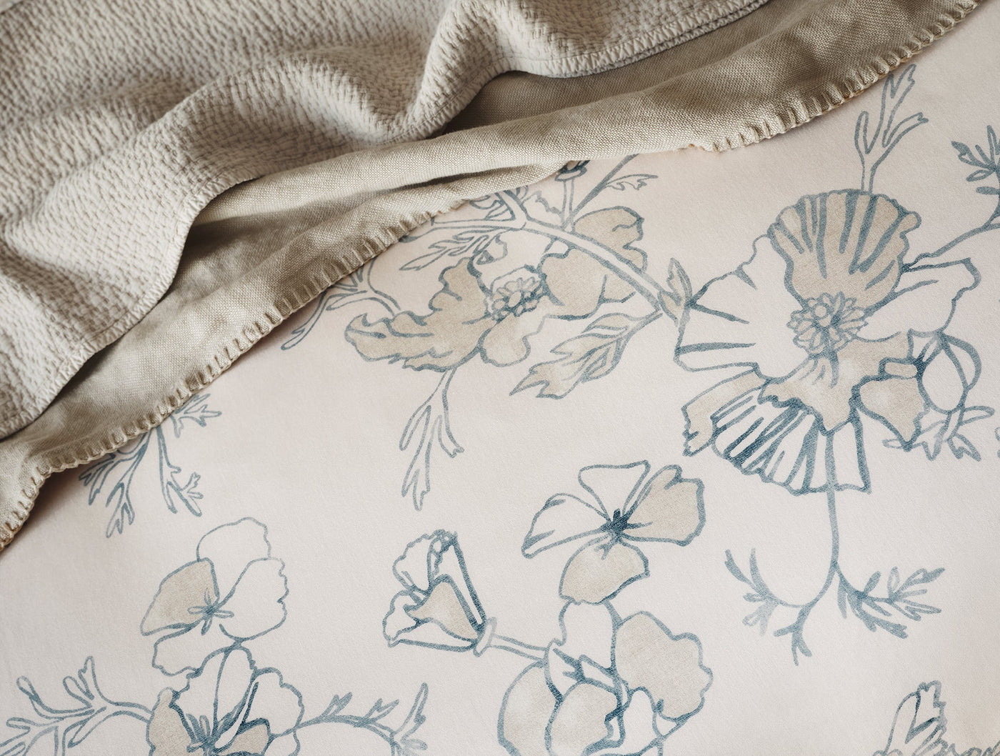 Close-up of Coyuchi Romneya Print duvet cover showing blue floral botanical print on ivory cotton.