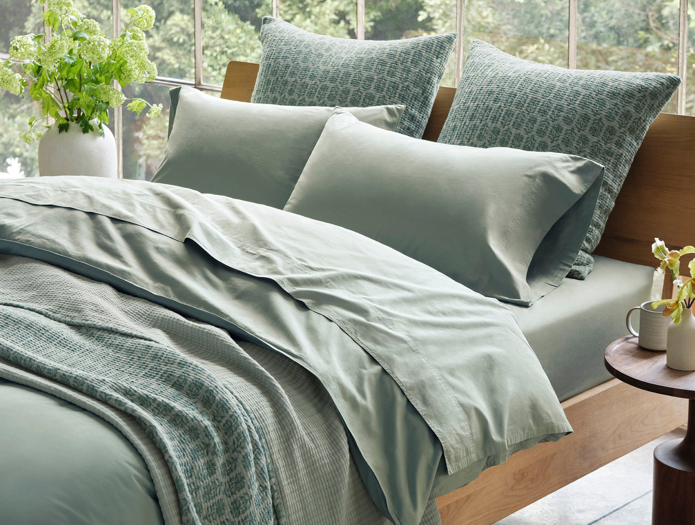 Close-up of Coyuchi Crinkled Percale sham in sage, styled with geometric-print shams on made bed.