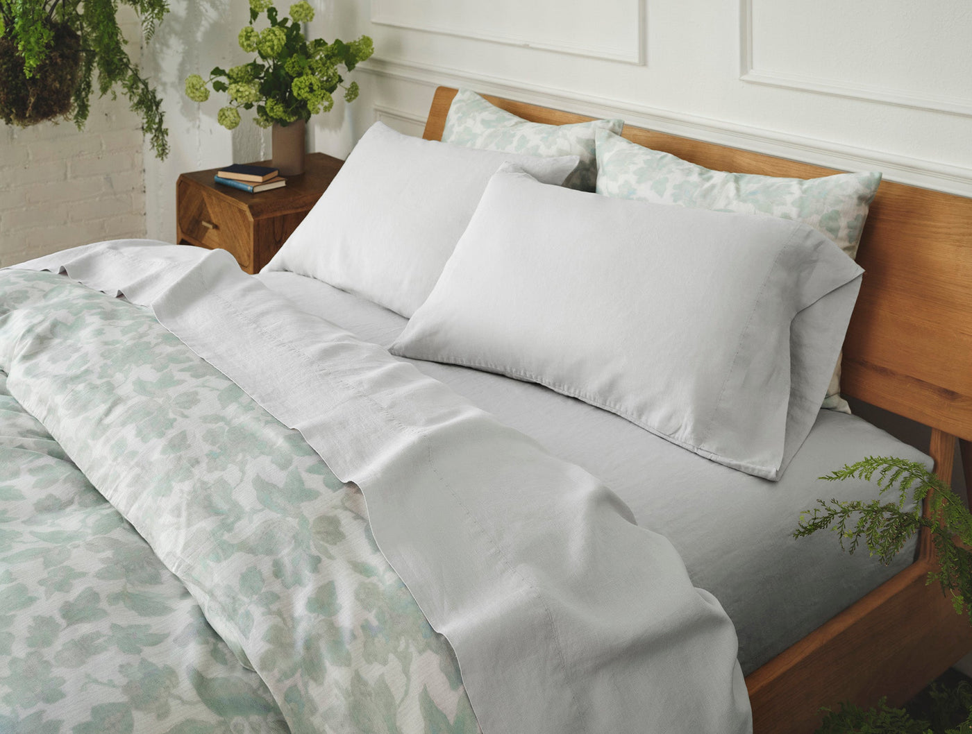 Soft white linen sheet set on wood bed with sage green floral duvet, natural bedroom setting.