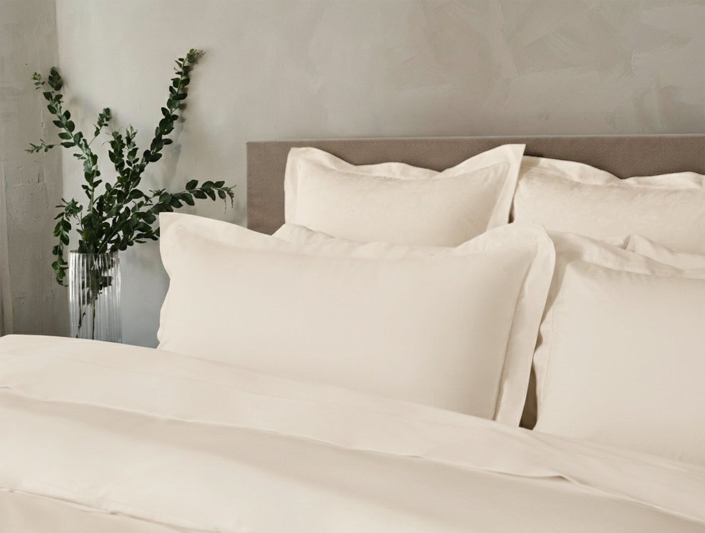 Close-up of ivory Coyuchi Heirloom Sateen shams stacked against a neutral headboard.