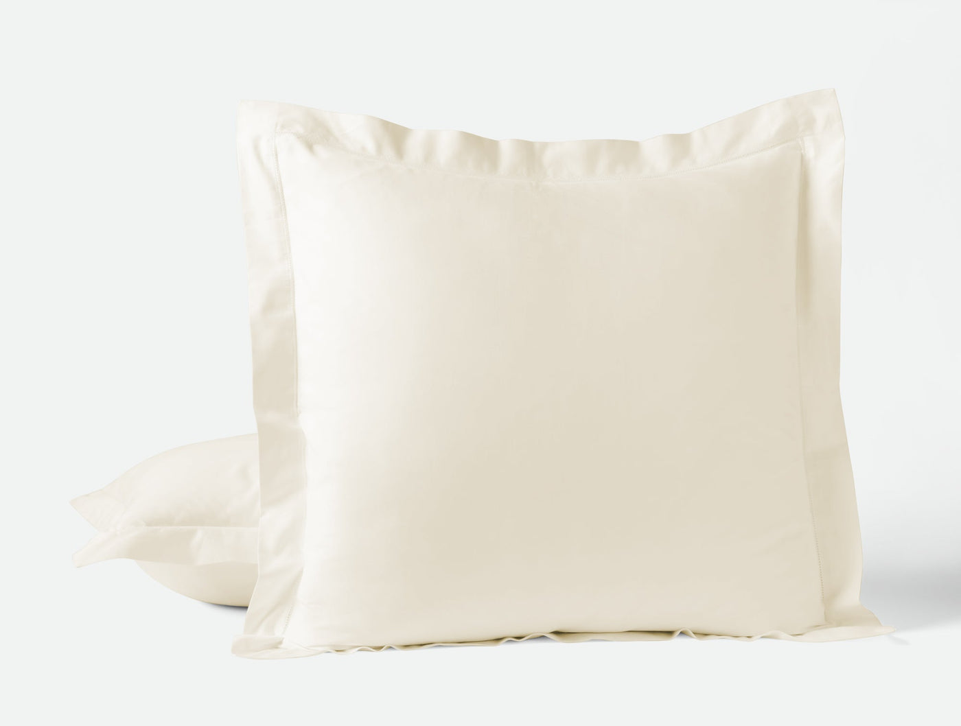 Ivory sateen pillow sham with flanged border, stacked pair on light background.
