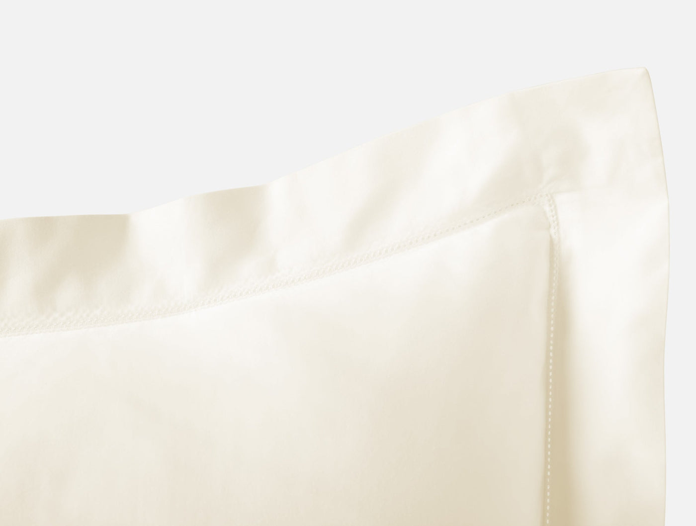 Close-up of ivory sateen pillow sham corner showing lustrous fabric and flanged edge.