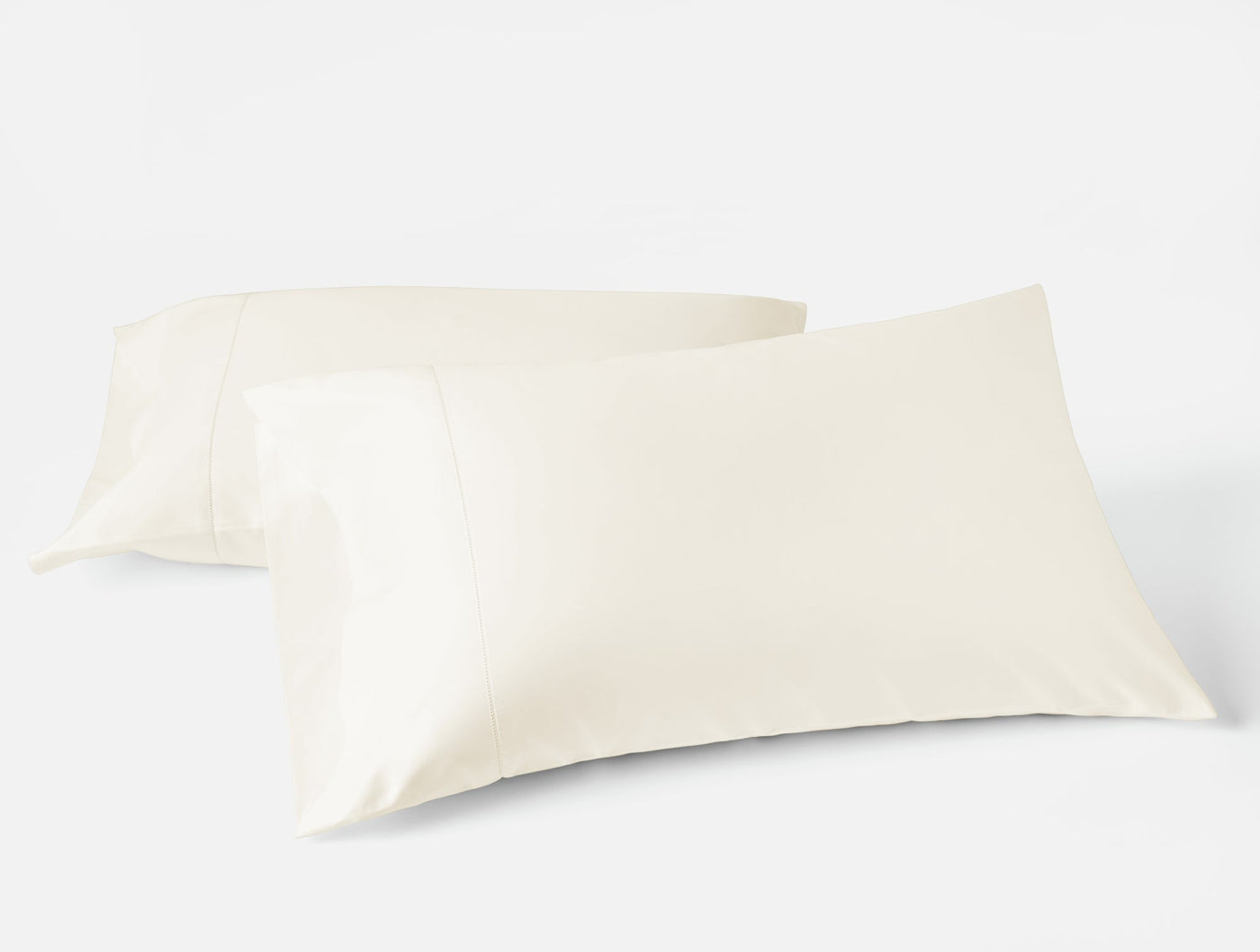 Two ivory Coyuchi Heirloom Sateen pillowcases stacked, showing smooth lustrous finish.