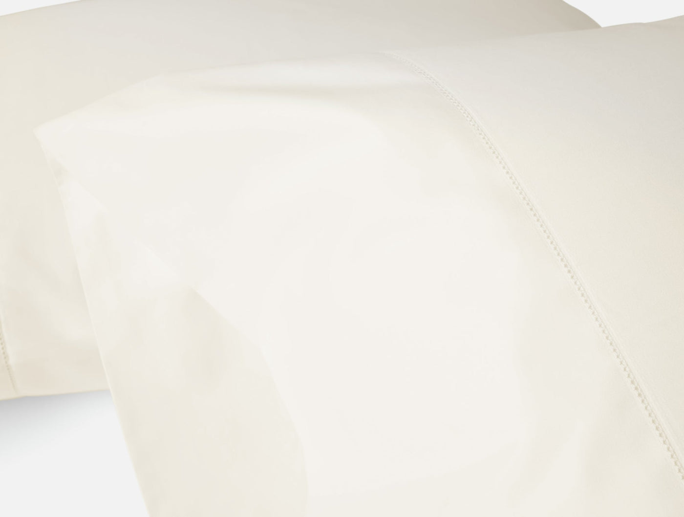 Close-up of ivory sateen sheet hem detail showing delicate stitching against smooth fabric.