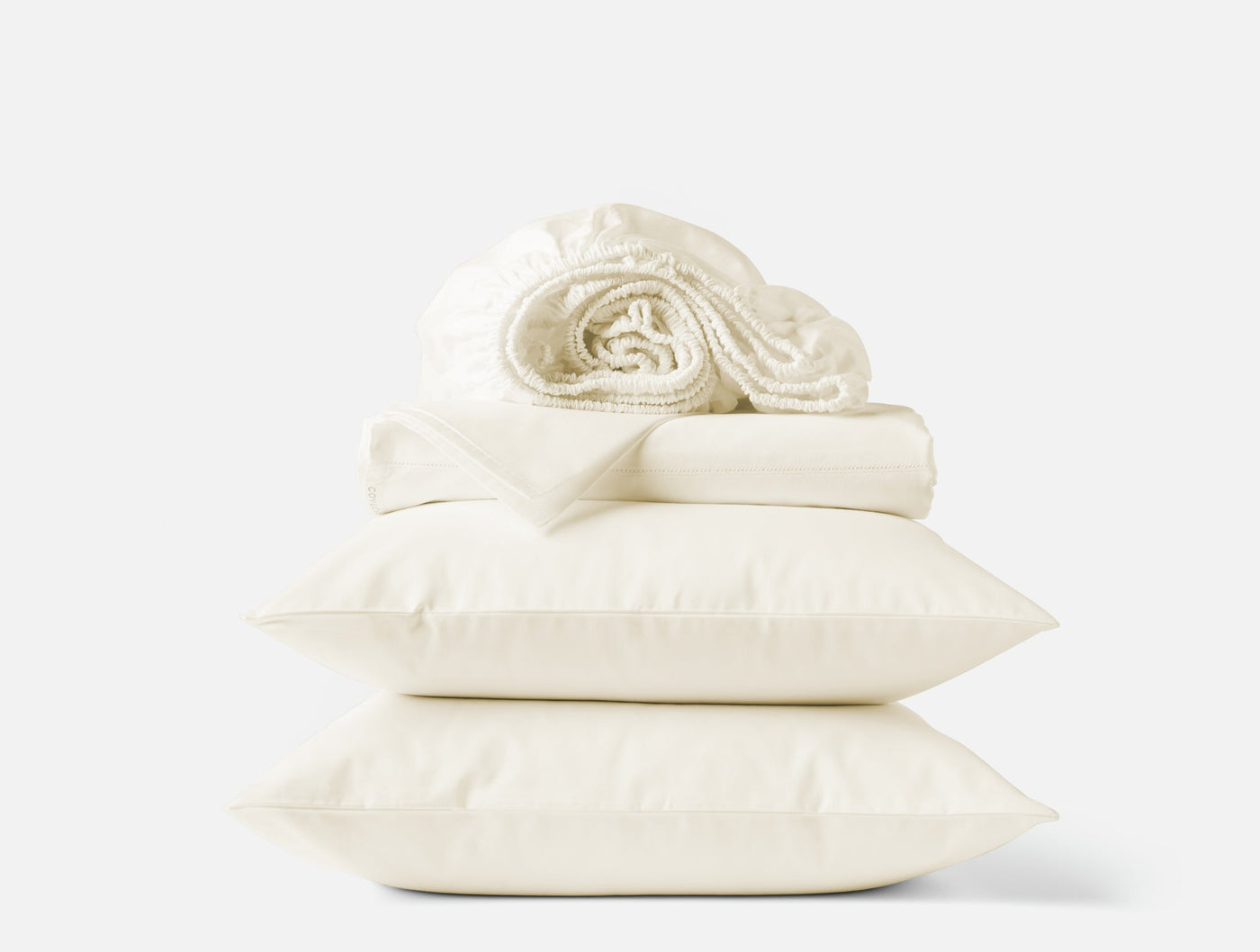 Ivory sateen sheet set stacked with two pillowcases and a rolled fitted sheet on top.