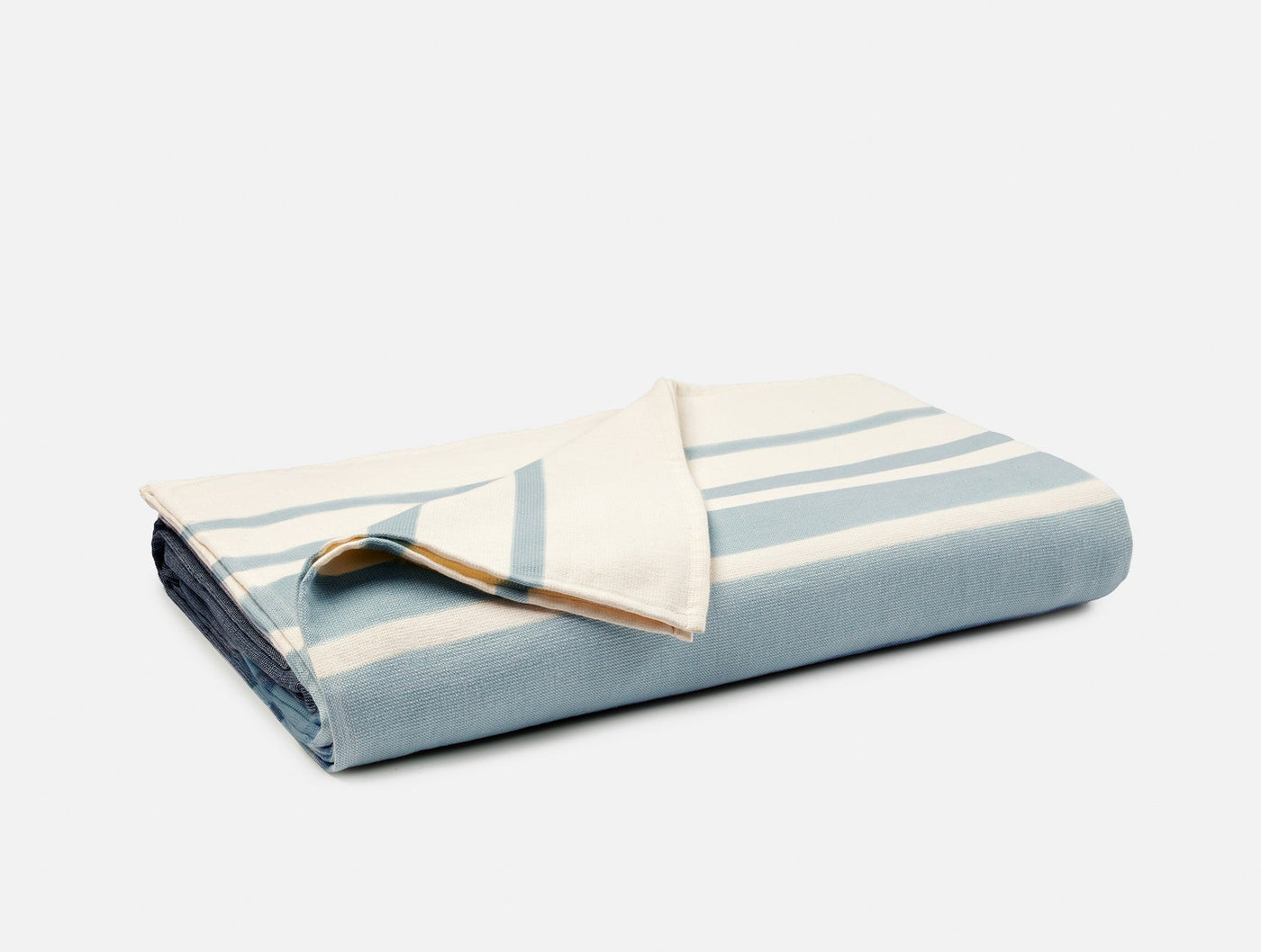 Folded Coyuchi Laguna beach blanket showing pale blue and ivory stripe pattern with corner turned back.