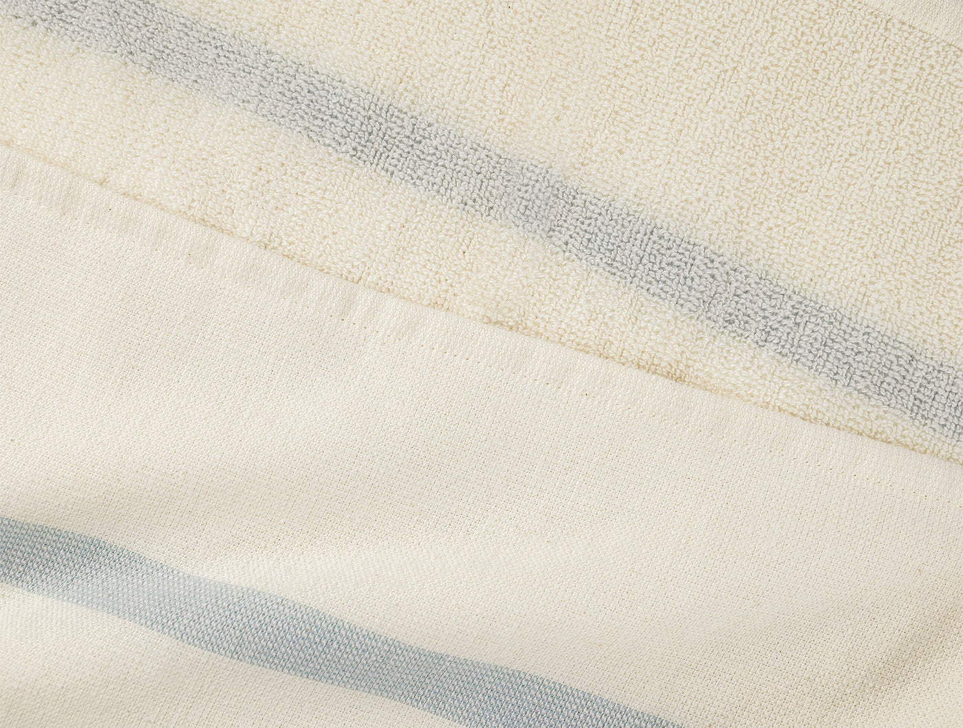 Close-up of ivory woven cotton beach blanket with pale blue stripes and visible hem fold.