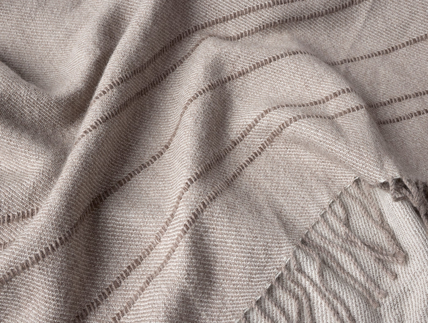 Close-up of taupe alpaca throw with tonal stripe weave and fringe edge detail.
