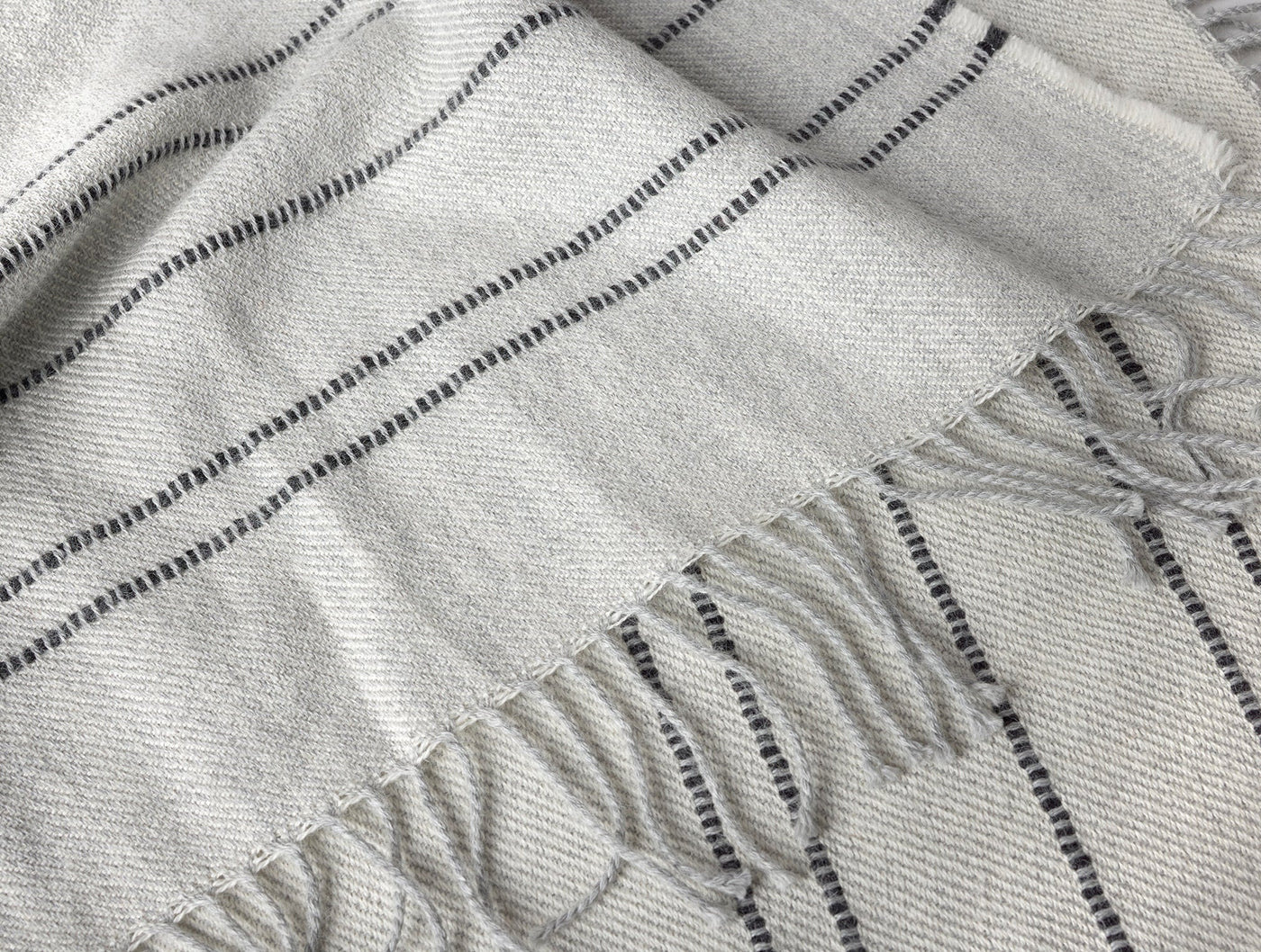 Close-up of Coyuchi Lima throw's fringe edge, showing ivory and charcoal stripe weave texture.