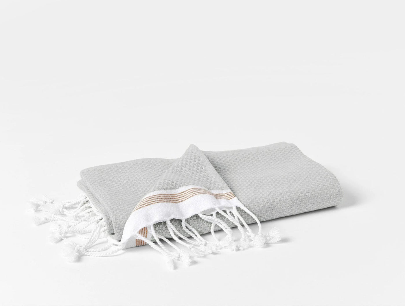 Close-up of folded silver Coyuchi Mediterranean bath sheet with white fringe and caramel stripe detail.