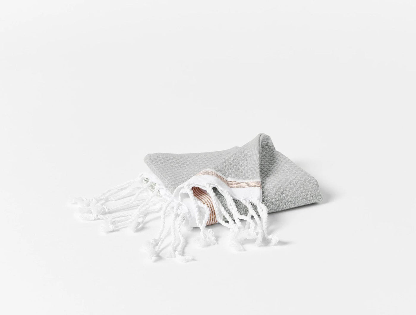 Coyuchi Mediterranean bath towel folded, pale grey waffle weave with terracotta stripe and white fringe.