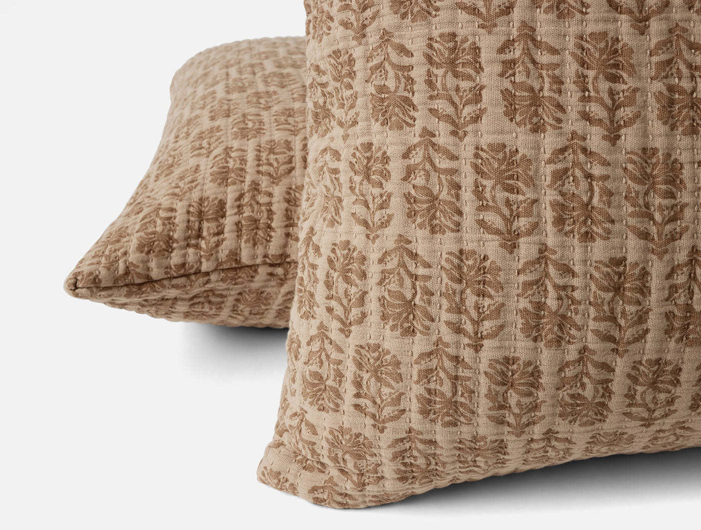 Close-up of two Coyuchi Mirada Matelassé shams in tan with tonal block-print floral pattern.