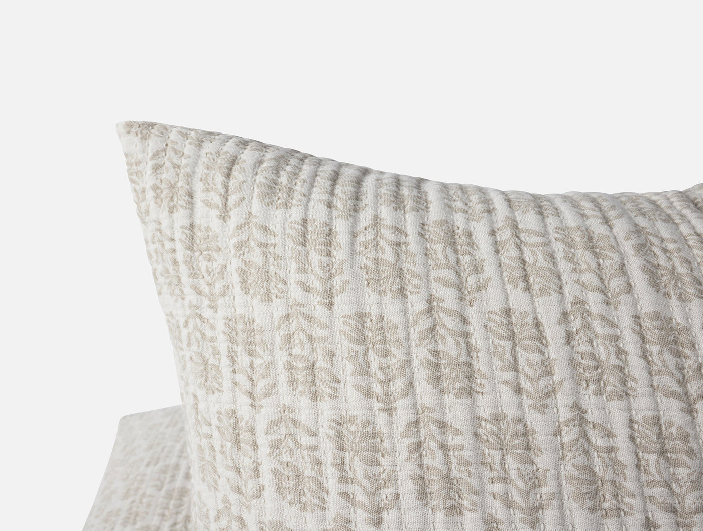 Close-up corner of Coyuchi Mirada Matelassé sham in ivory with taupe floral block print.