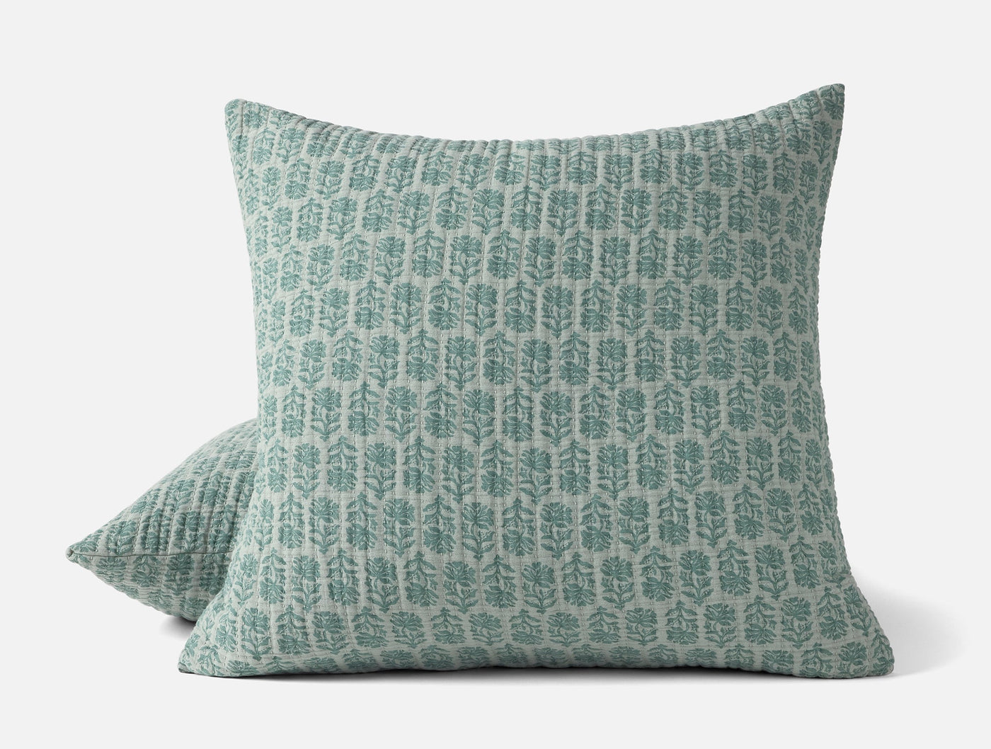 Close-up of two Coyuchi Mirada Matelassé shams in sage with block-print botanical motif.