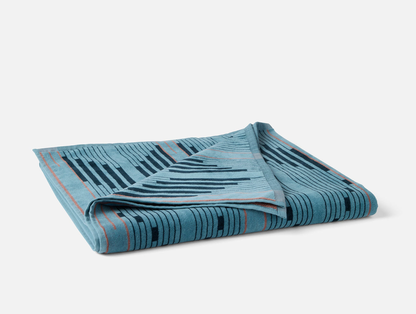 Folded teal Coyuchi Morelia beach towel showing geometric stripe pattern with coral trim detail.