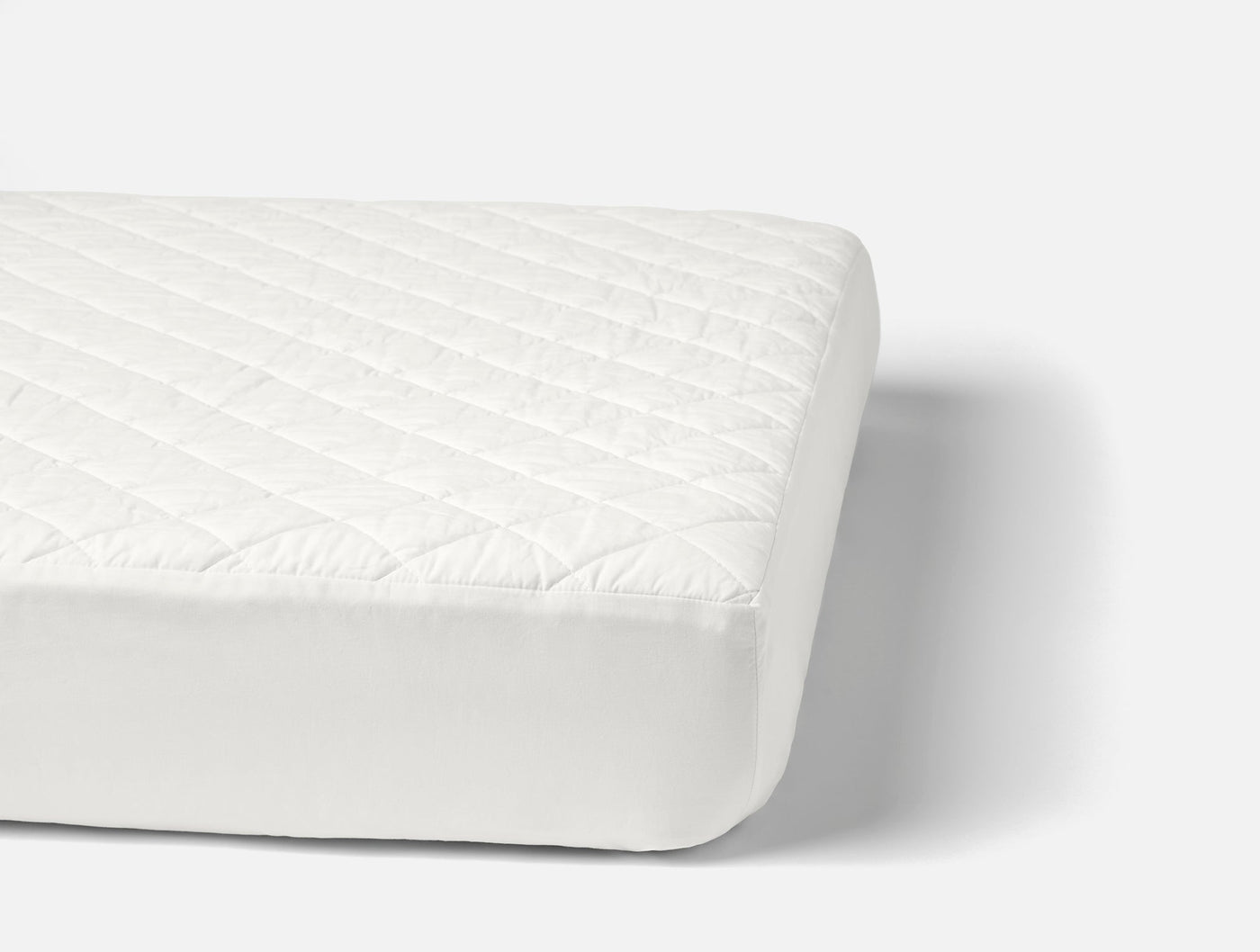 Angled view of Coyuchi ivory quilted cotton mattress pad fitted on mattress.