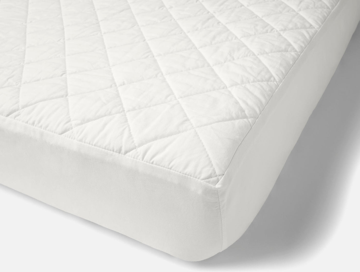 Angled view of white quilted cotton mattress pad fitted on a mattress corner.
