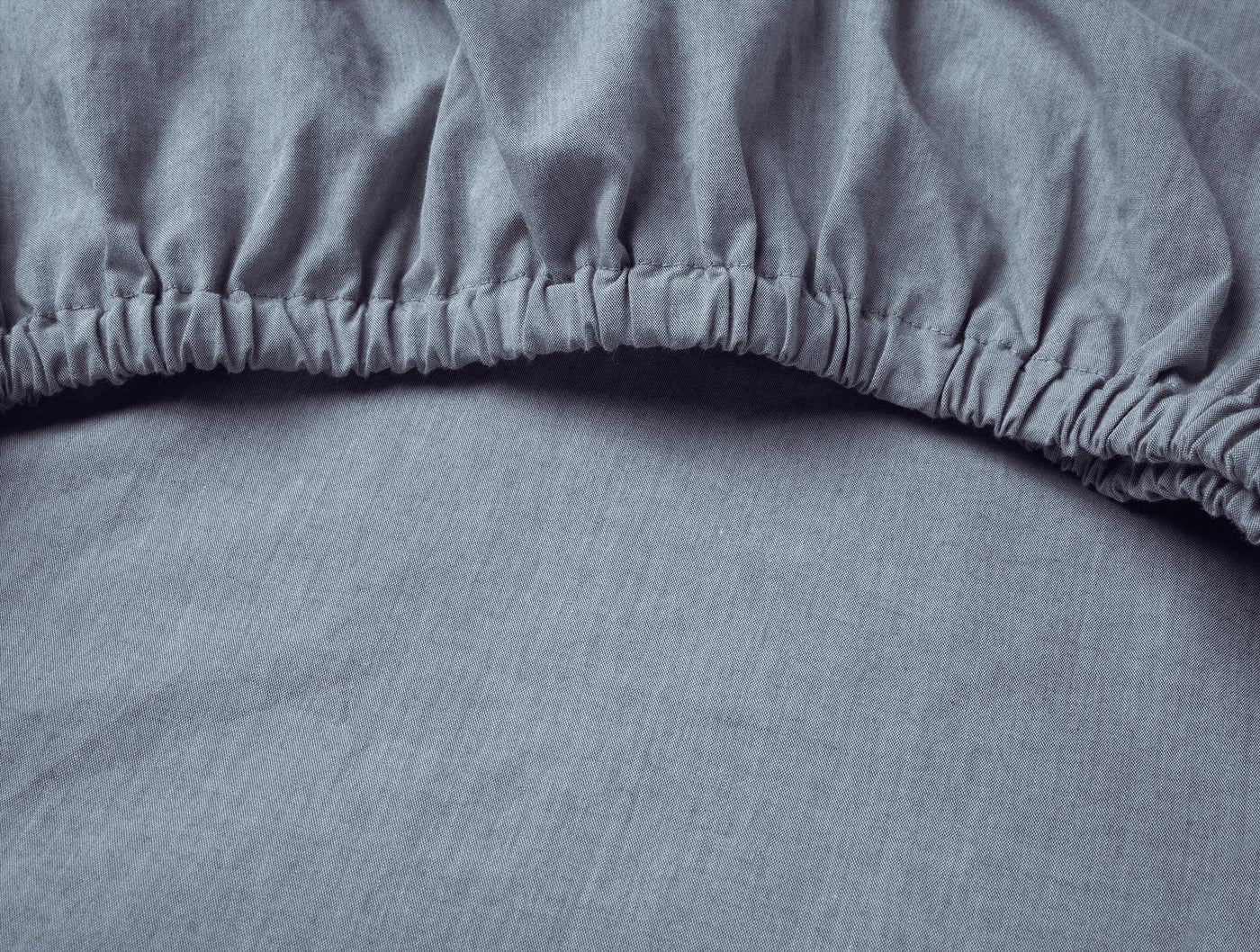Close-up of Coyuchi Crinkled Percale fitted sheet elasticized corner in slate blue.