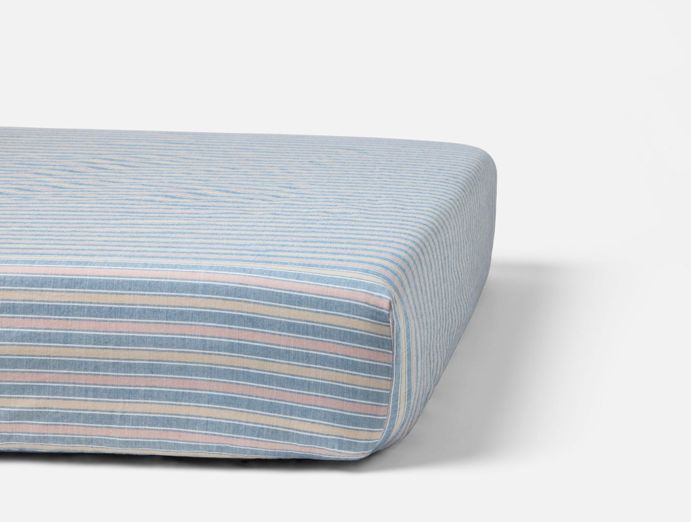 Corner detail of Coyuchi Crinkled Percale fitted sheet in multicolor pastel stripes on a mattress.