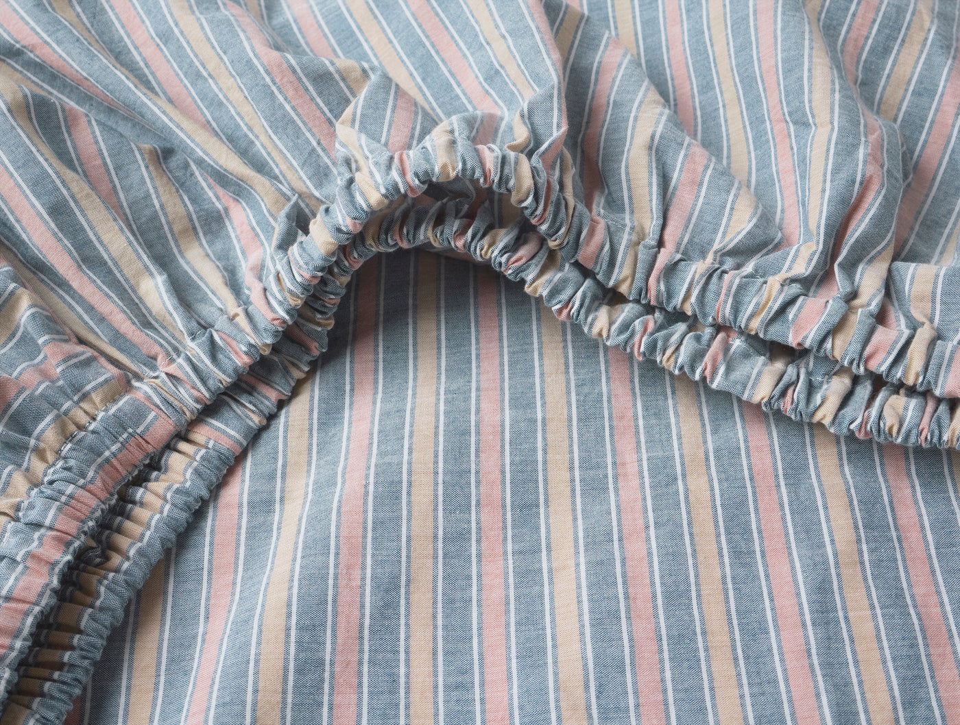 Close-up of elasticated corner on a crinkled percale fitted sheet with multicolor stripes.