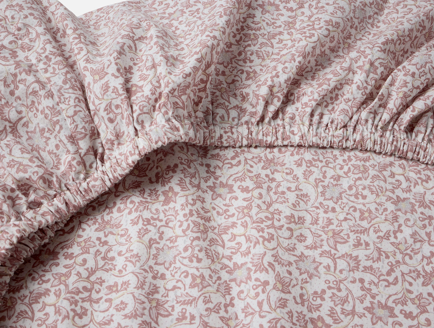 Close-up of Coyuchi fitted sheet corner showing elasticated edge with rose floral percale print.