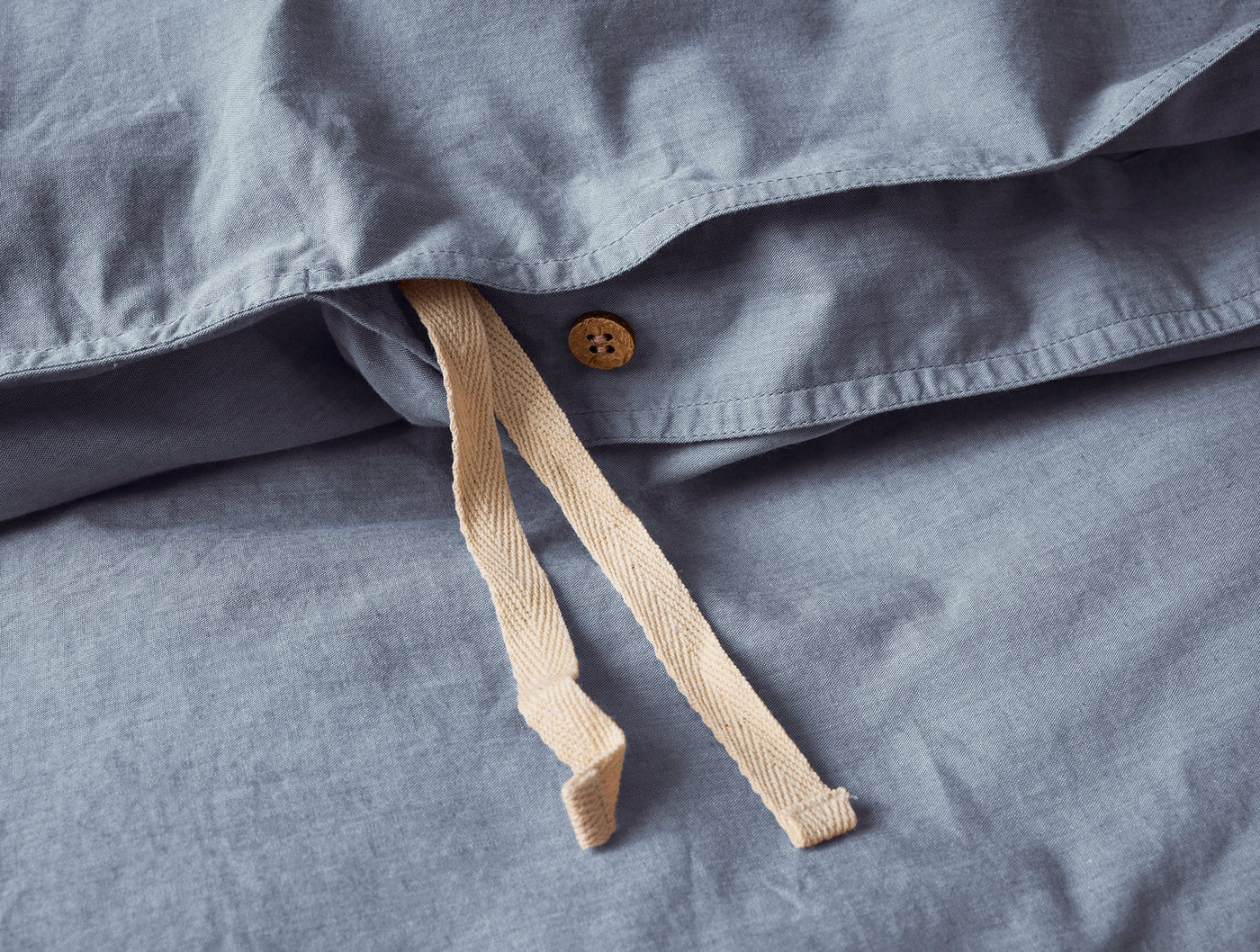Close-up of slate blue duvet cover closure with wooden button and natural cotton ties.