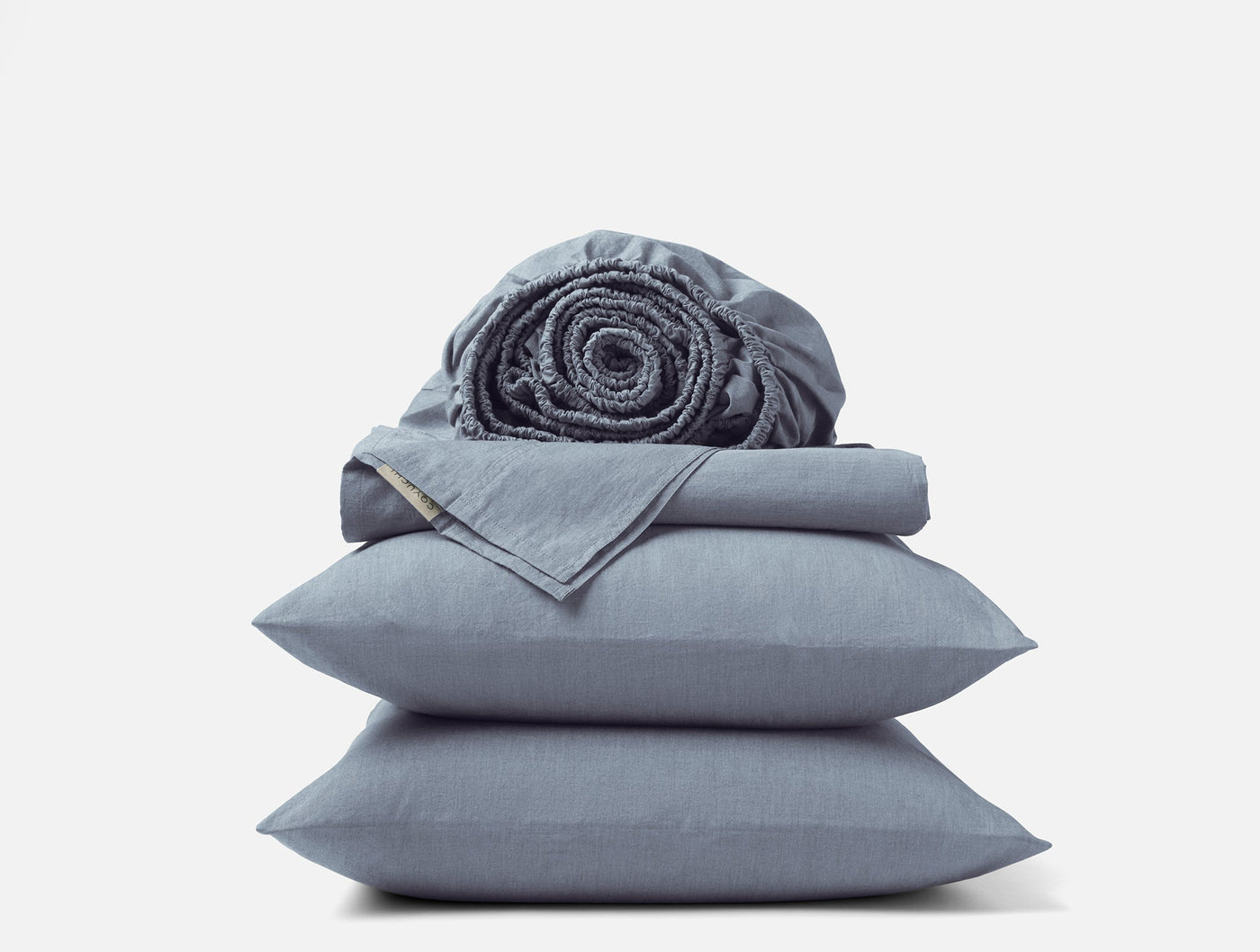 Stacked slate blue Coyuchi Crinkled Percale pillowcases and sheets with a rolled fitted sheet on top.