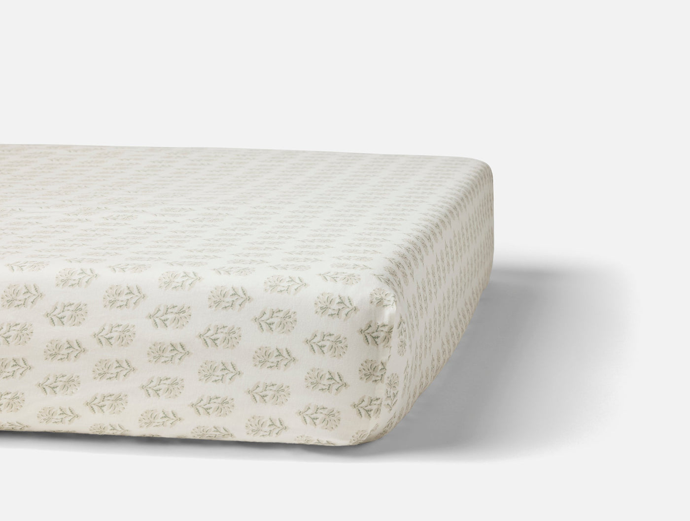 Angled view of fitted sheet on mattress, sage block-print botanical motif on ivory percale.