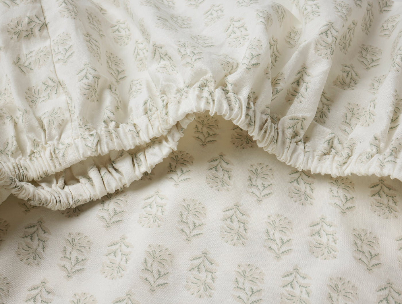 Close-up of ivory fitted sheet corner showing elasticated edge and sage green floral block print.