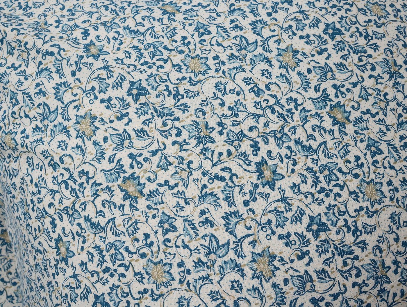 Close-up of ivory percale fabric with intricate blue and gold floral vine print.