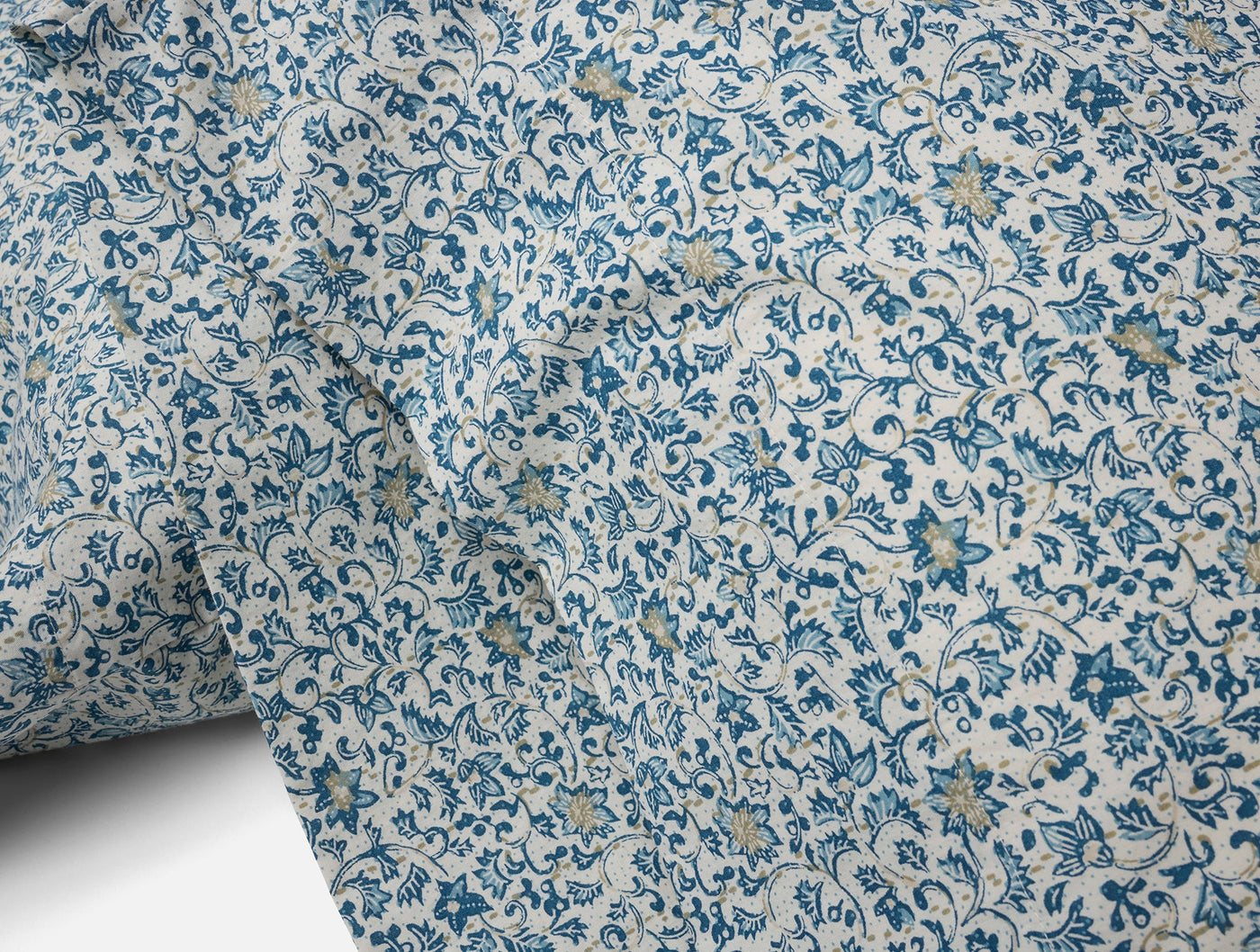 Close-up of Coyuchi Print Percale pillowcase fabric, blue floral vine pattern on ivory.