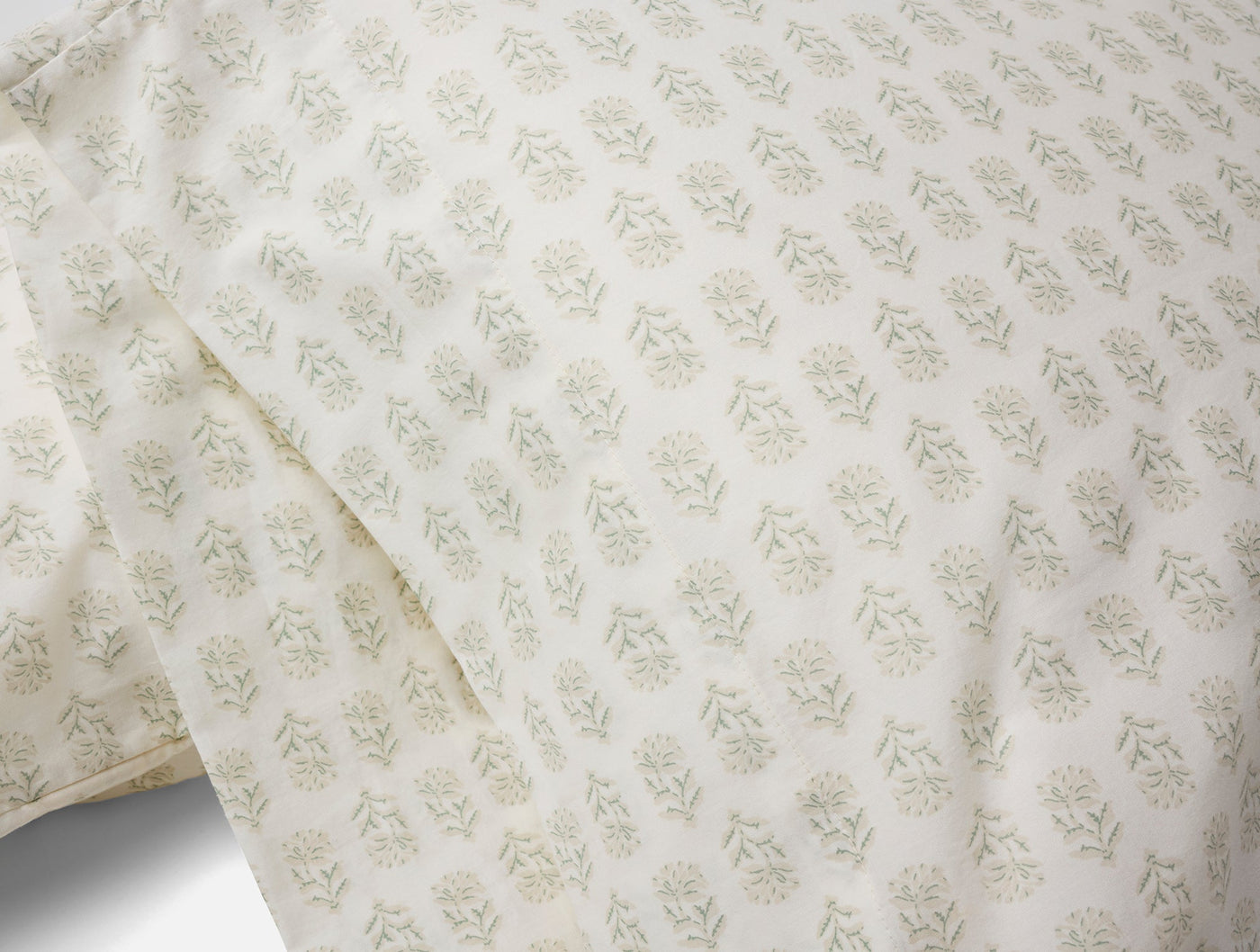 Close-up of ivory percale pillowcases with sage green floral block-print motifs.