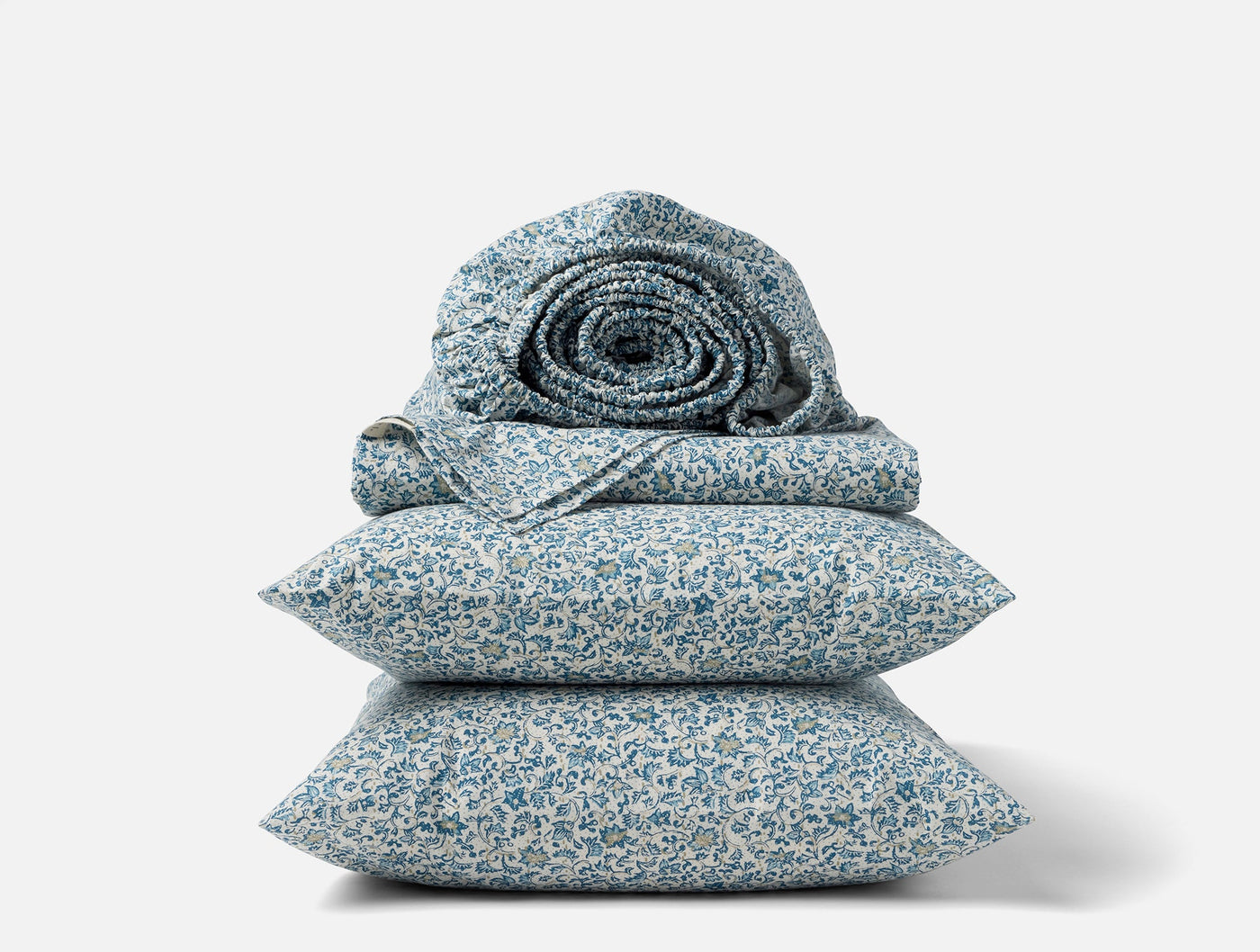 Close-up of stacked Coyuchi Print Percale sheet set in blue floral pattern with rolled duvet on top.