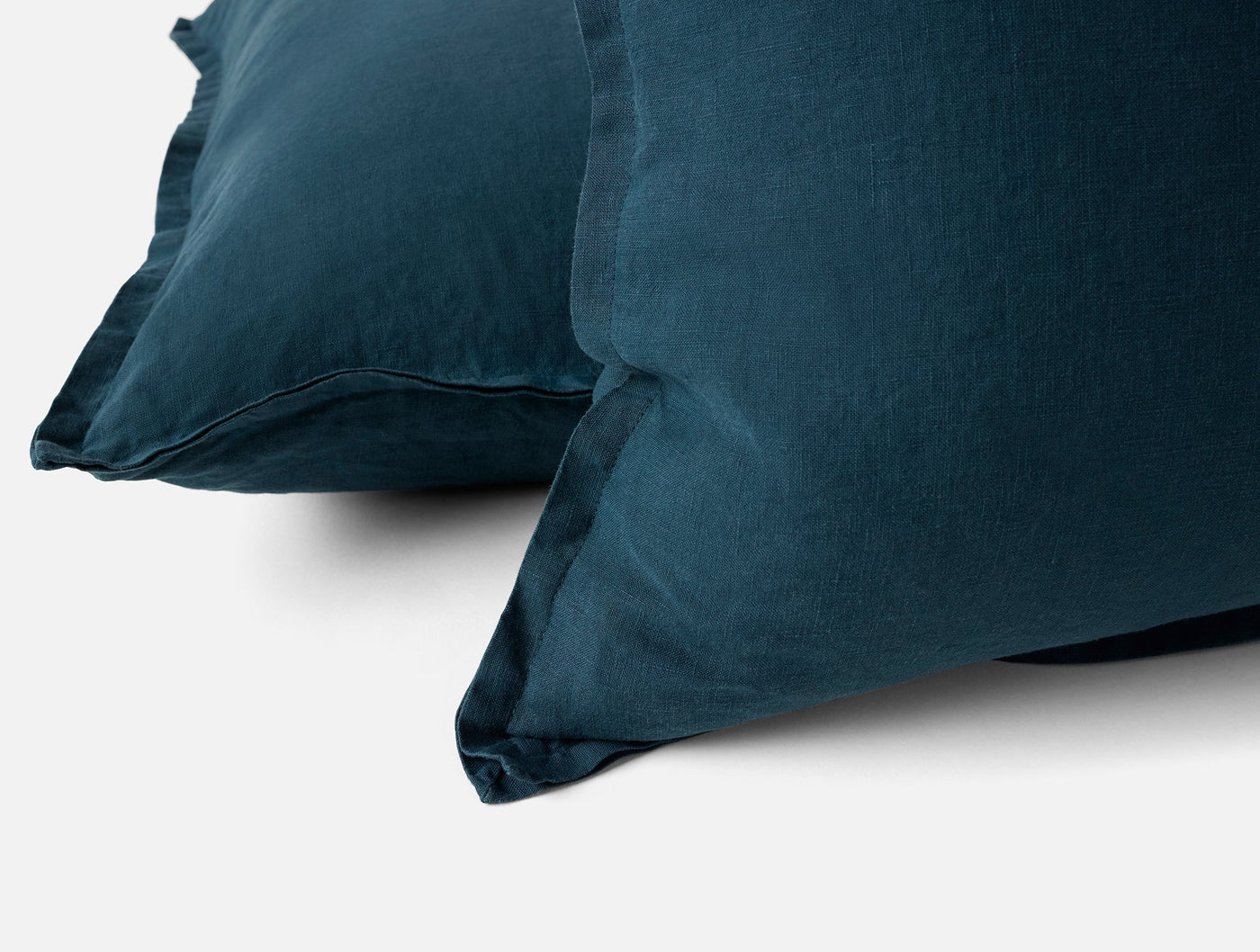 Close-up of two Coyuchi Relaxed Linen pillow covers in deep teal with frayed edges.