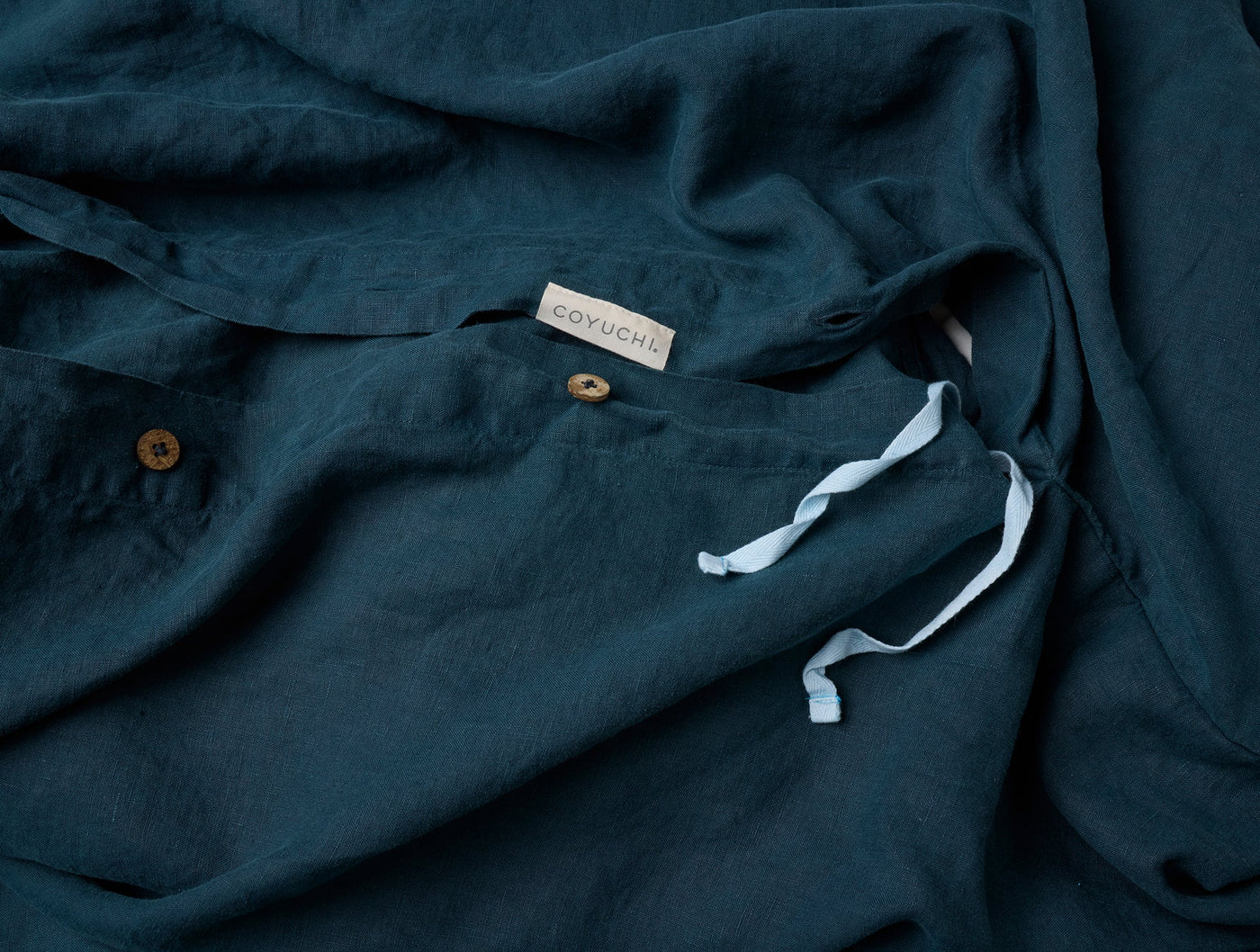 Close-up of Coyuchi Relaxed Linen duvet cover in teal, showing label, buttons, and ties.