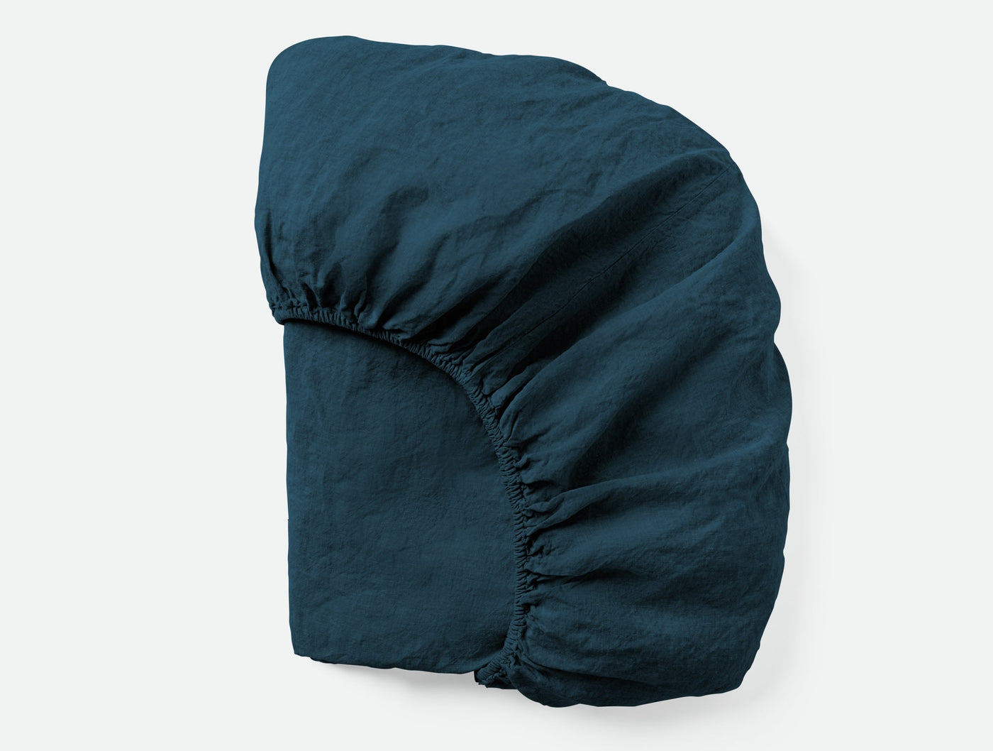 Coyuchi Relaxed Linen fitted sheet in deep teal, folded to show elasticised corners.