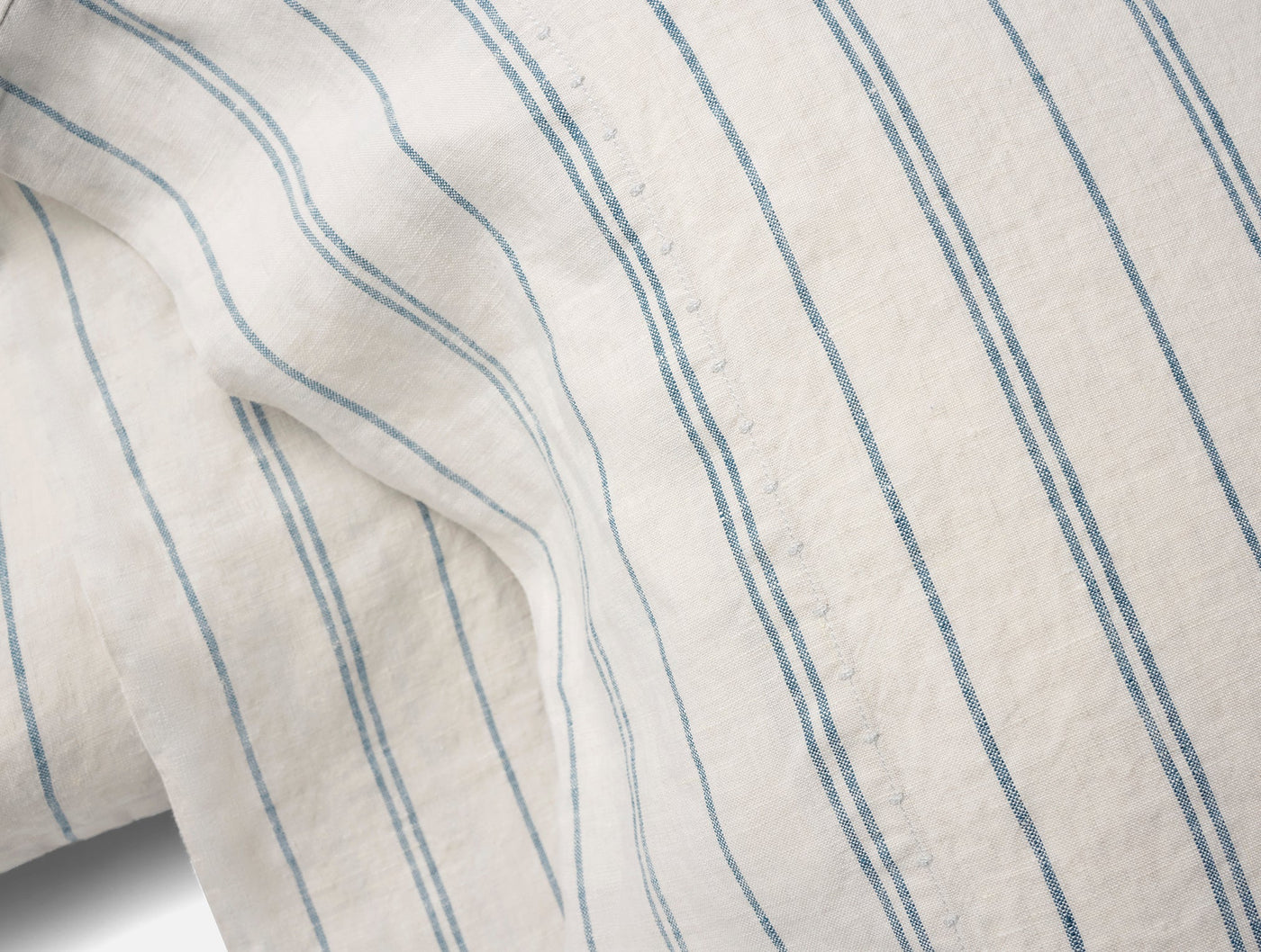 Close-up of Coyuchi Relaxed Linen pillowcase in white with blue pinstripes, showing soft drape.
