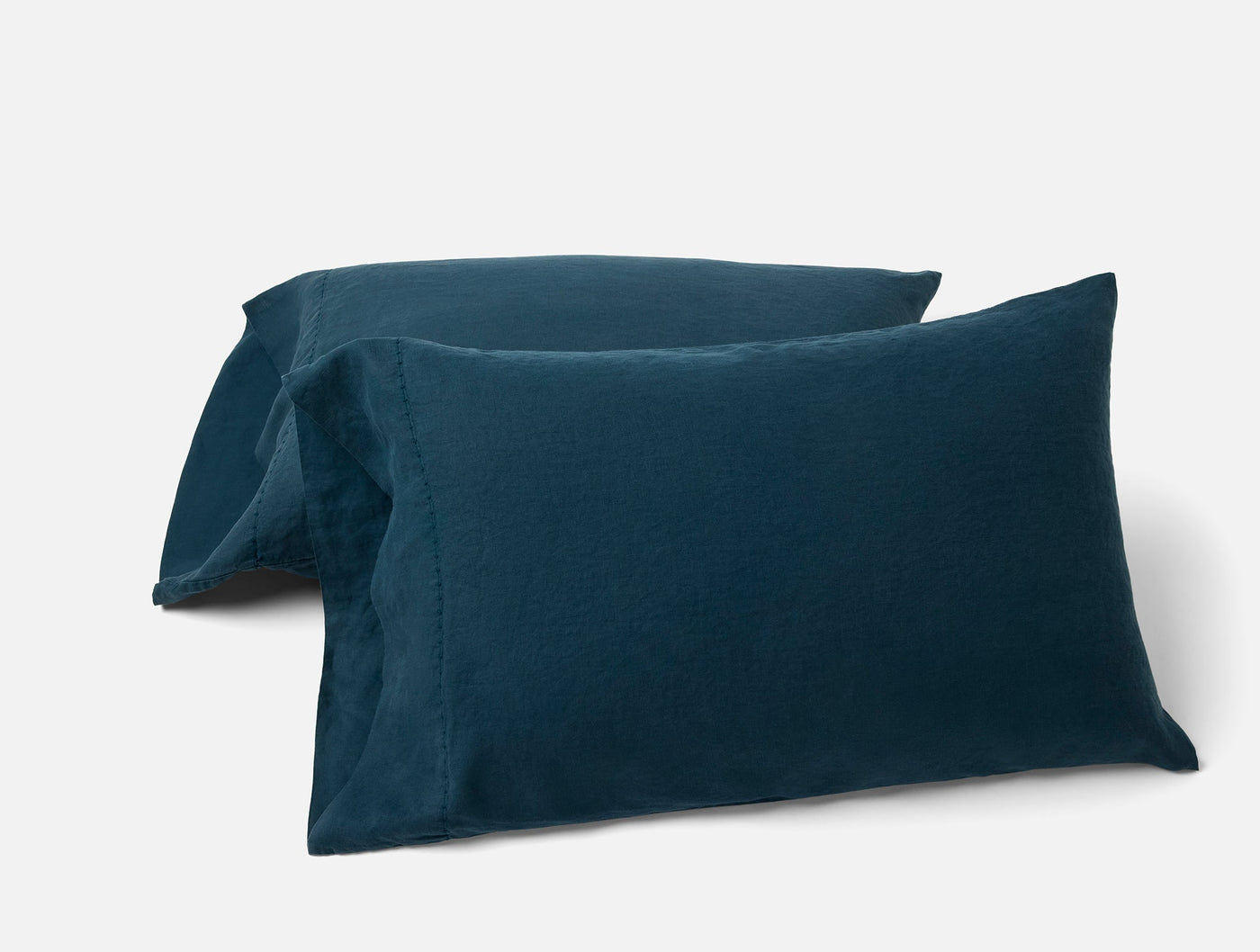 Close-up of two Coyuchi Relaxed Linen pillowcases in deep teal, stacked on white background.