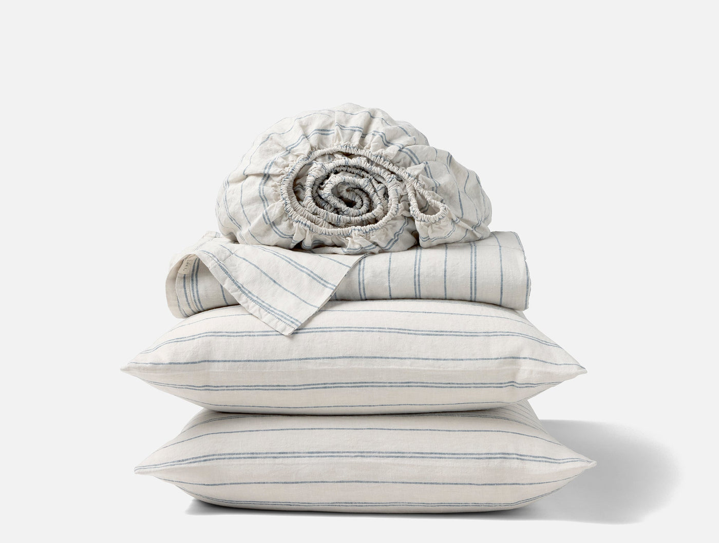 Stacked ivory linen sheet set with blue ticking stripes, rolled fitted sheet on top.