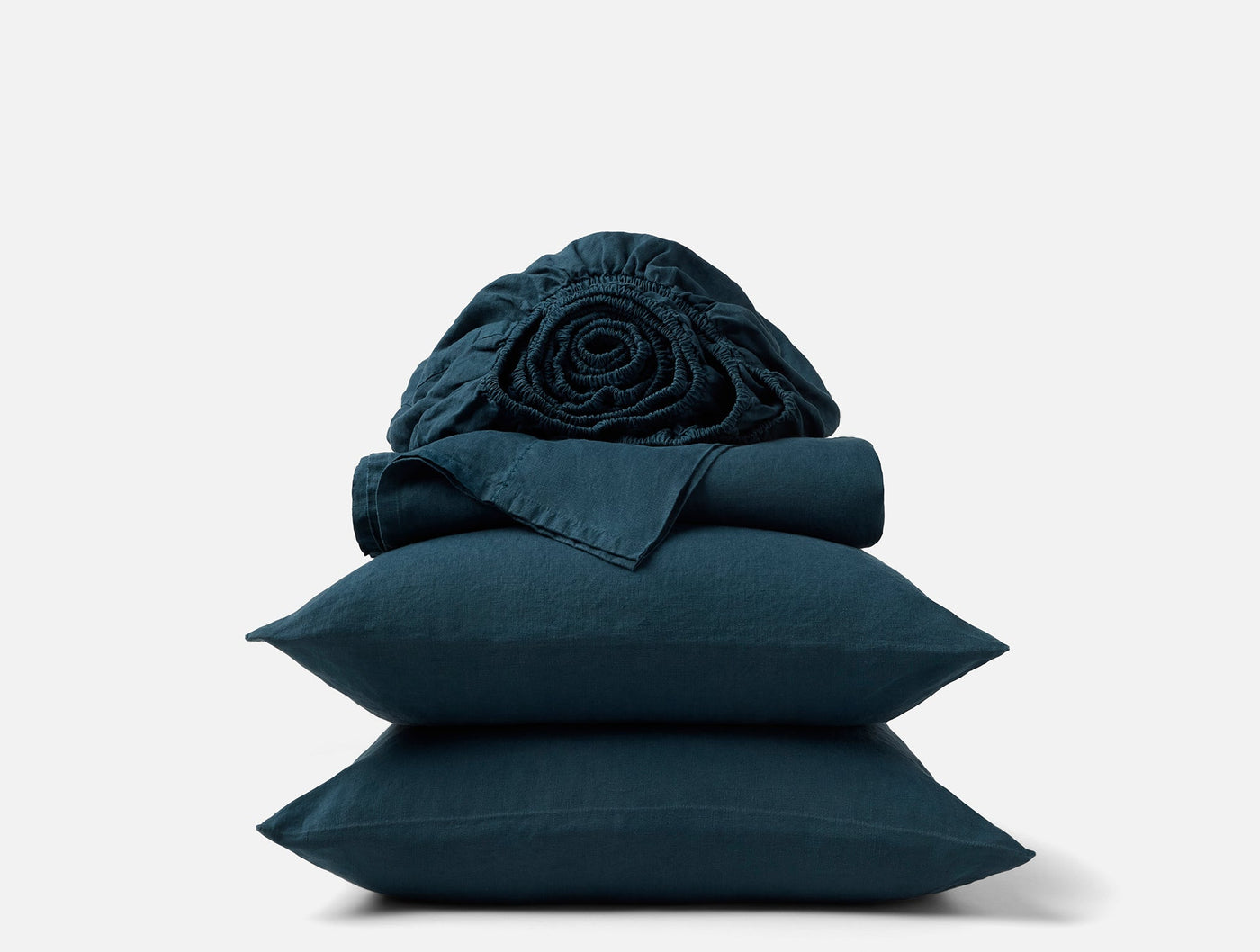Stacked teal linen pillowcases and sheets with a loosely rolled fitted sheet on top.