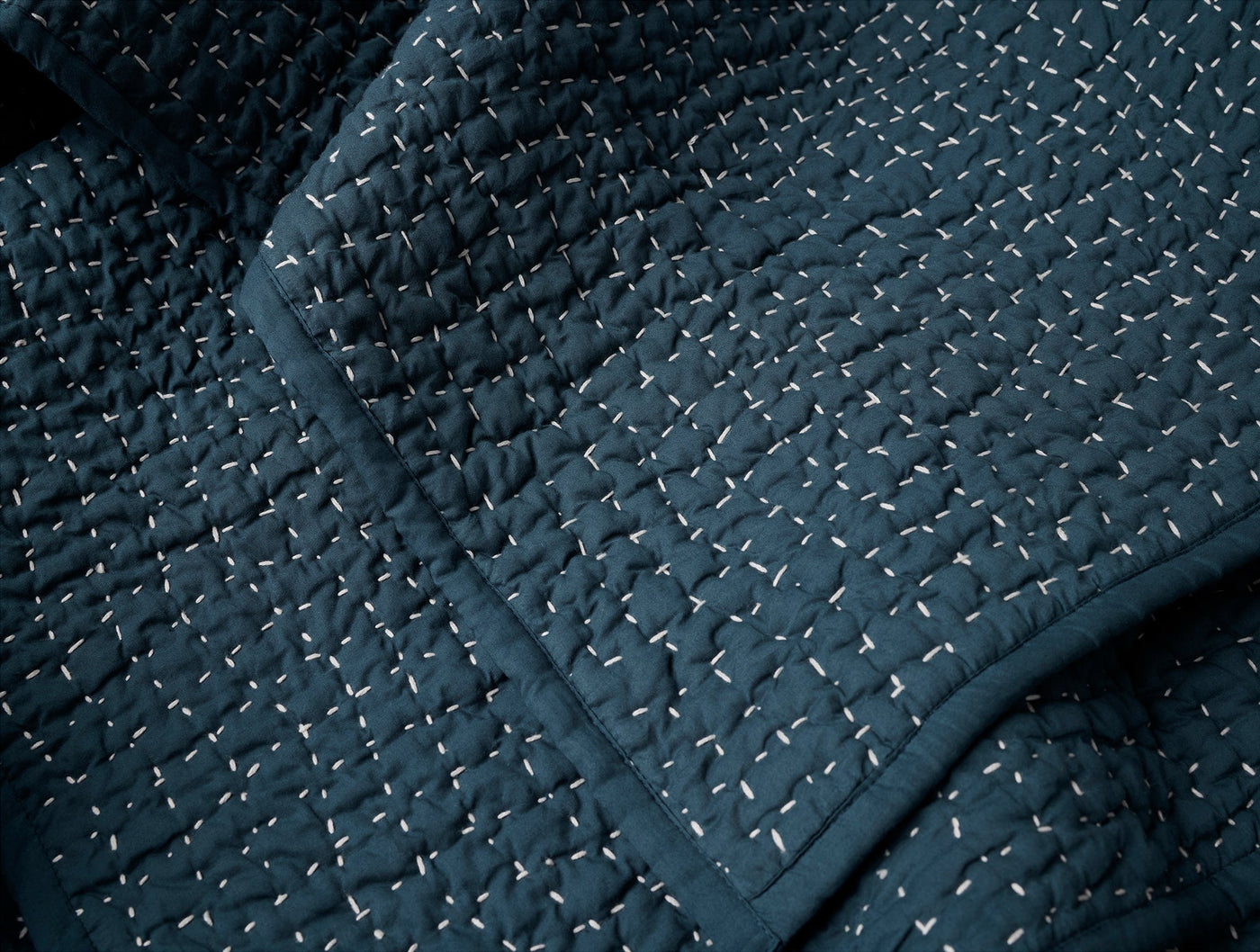 Close-up of navy Coyuchi quilt showing irregular white hand-stitching and quilted texture detail.