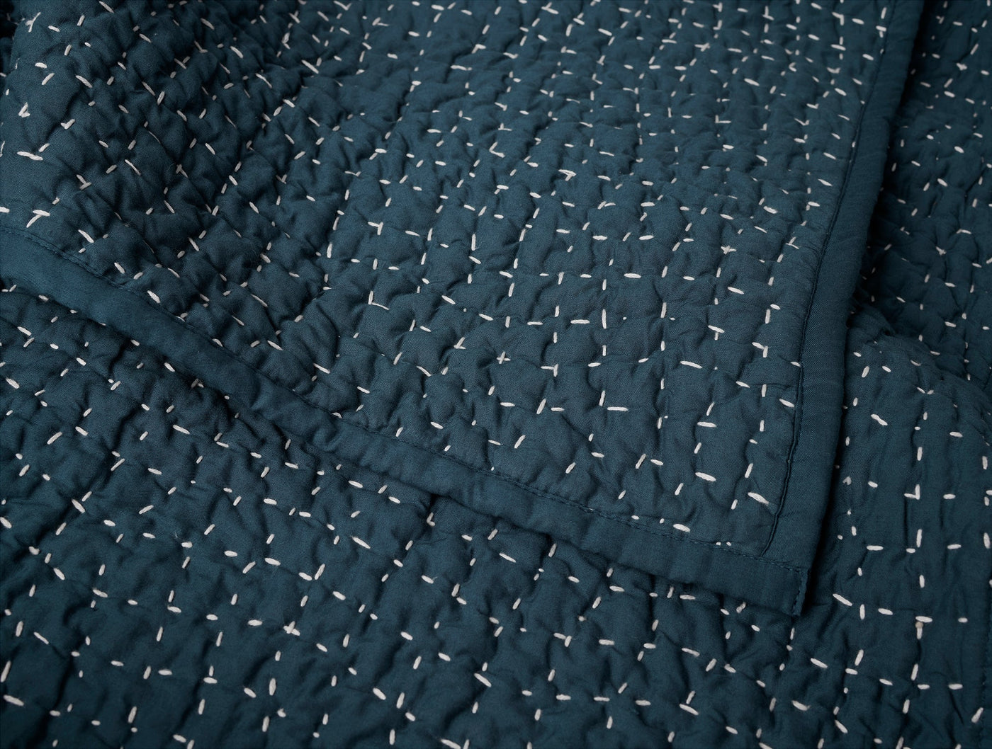 Close-up of Coyuchi Pebbled Handstitched quilt in deep navy with ivory hand-stitching detail.