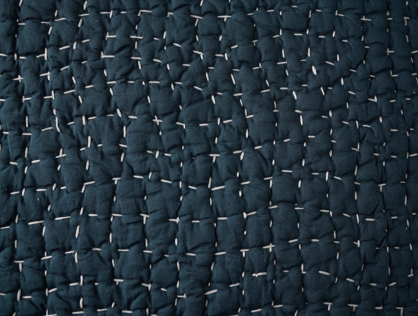 Close-up of navy blue pebbled linen sham with white hand-stitching detail.